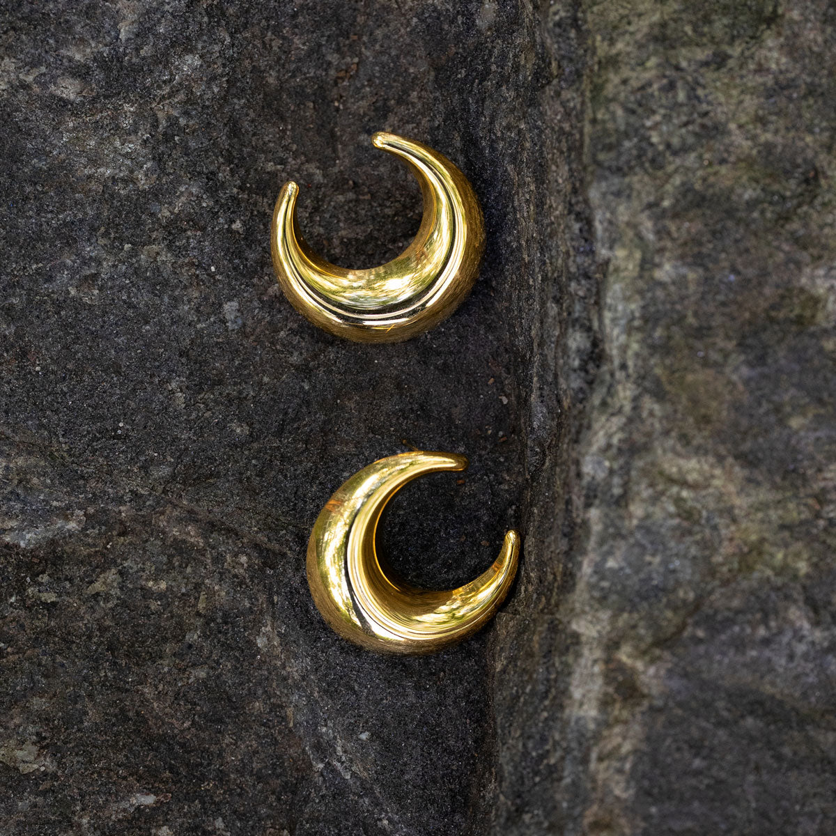 Gold crescent moon earrings on a dark stone surface
