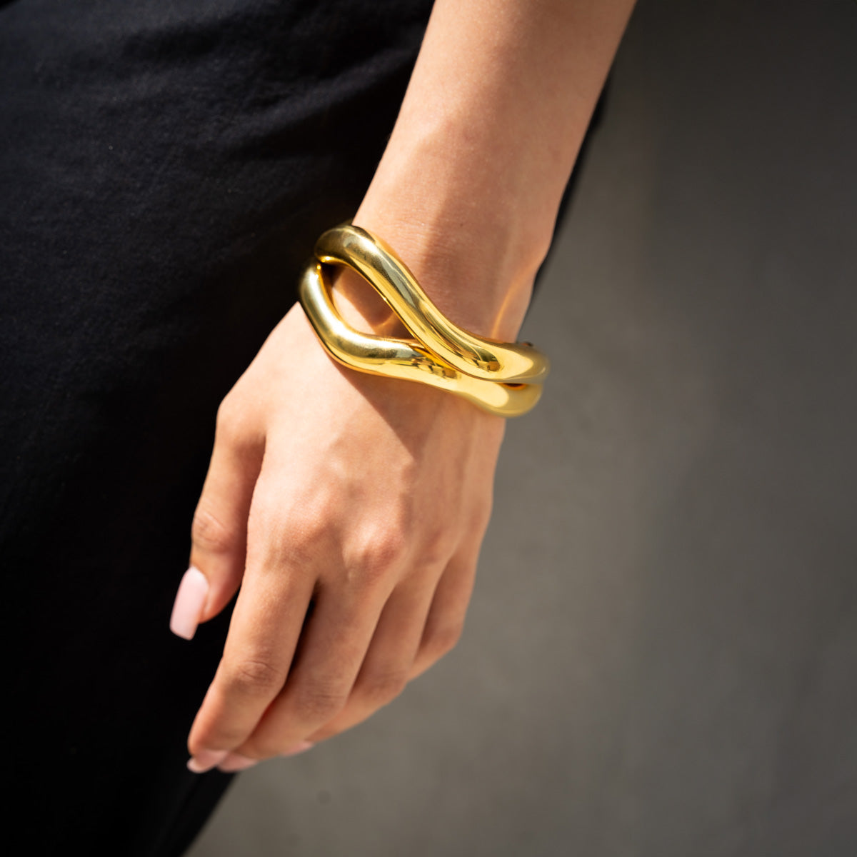 Golden fluid shaped glossy finish bracelet in set of two on a woman's wrist on a black summer dress