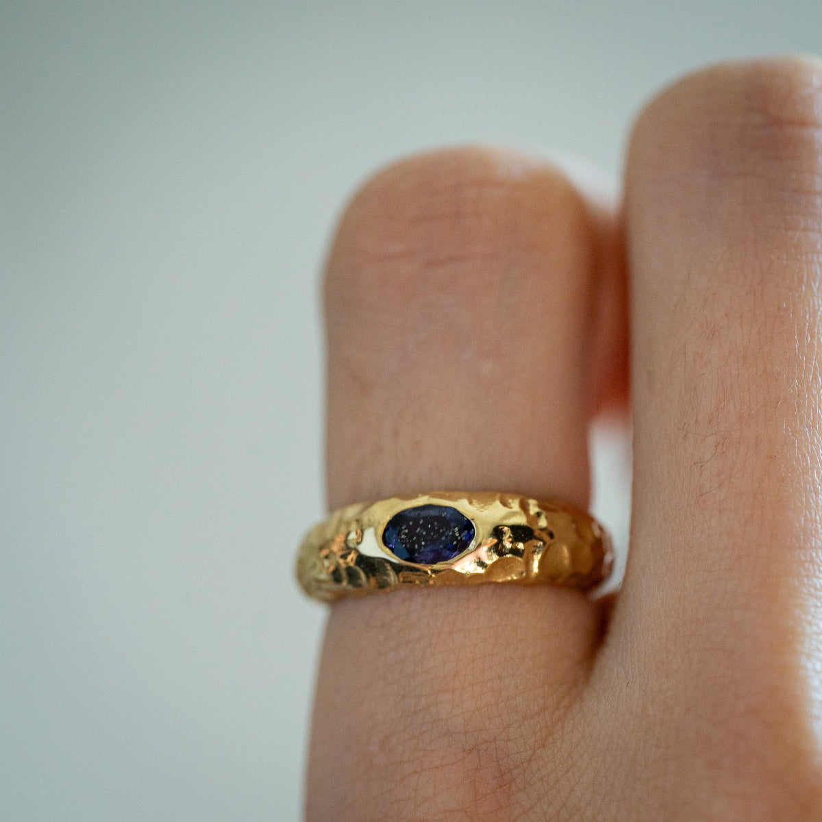 Gold plated textured glossy ring with a blue ionite stone on a finger