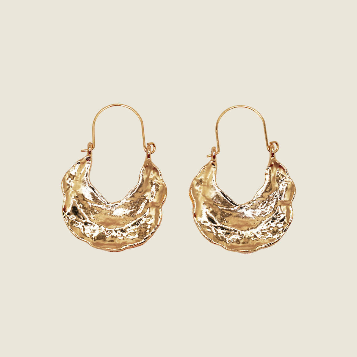 Pair of golden textured hoop earrings on a beige background