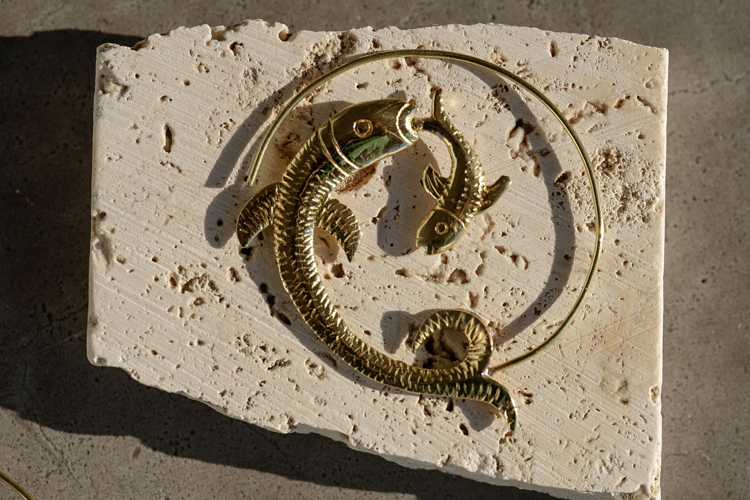 Golden fish hoop earring named Dancing Siren kept on a textured surface