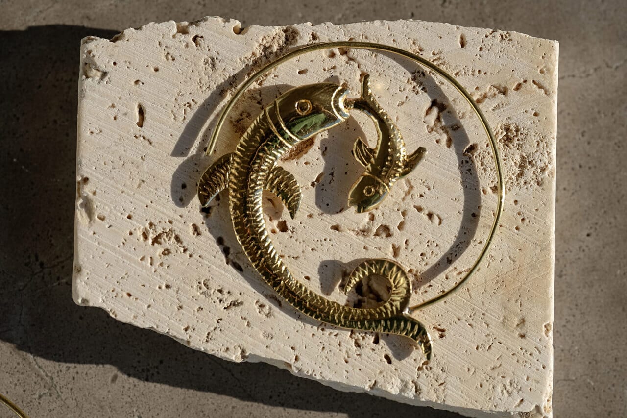 Golden fish hoop earring named Dancing Siren kept on a textured surface