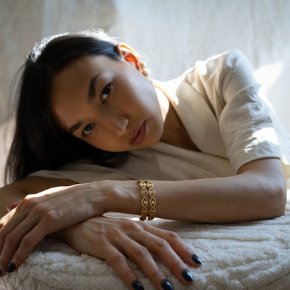 Woman wearing a eye shaped gold plated glossy finish bracelet set of two on a light background