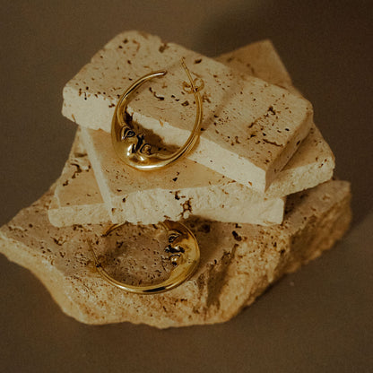 Pair of crescent face hoop earrings kept on stone