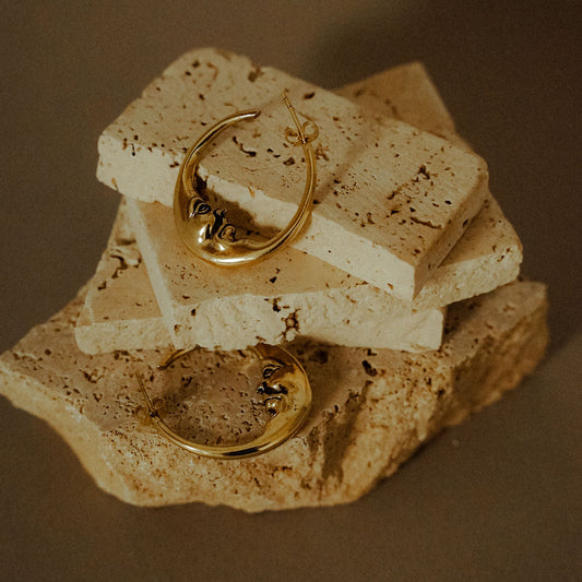 Pair of crescent face hoop earrings kept on stone