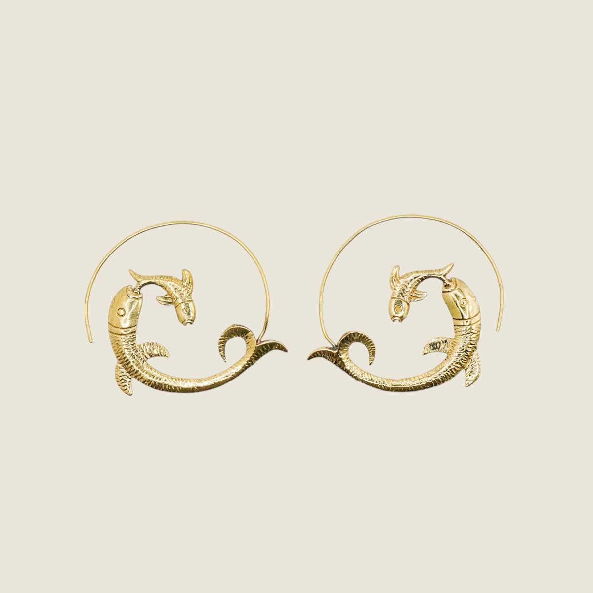 Golden brass fish-shaped hoop earrings on a beige background