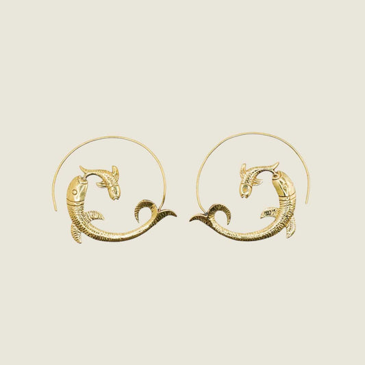Golden brass fish-shaped hoop earrings on a beige background