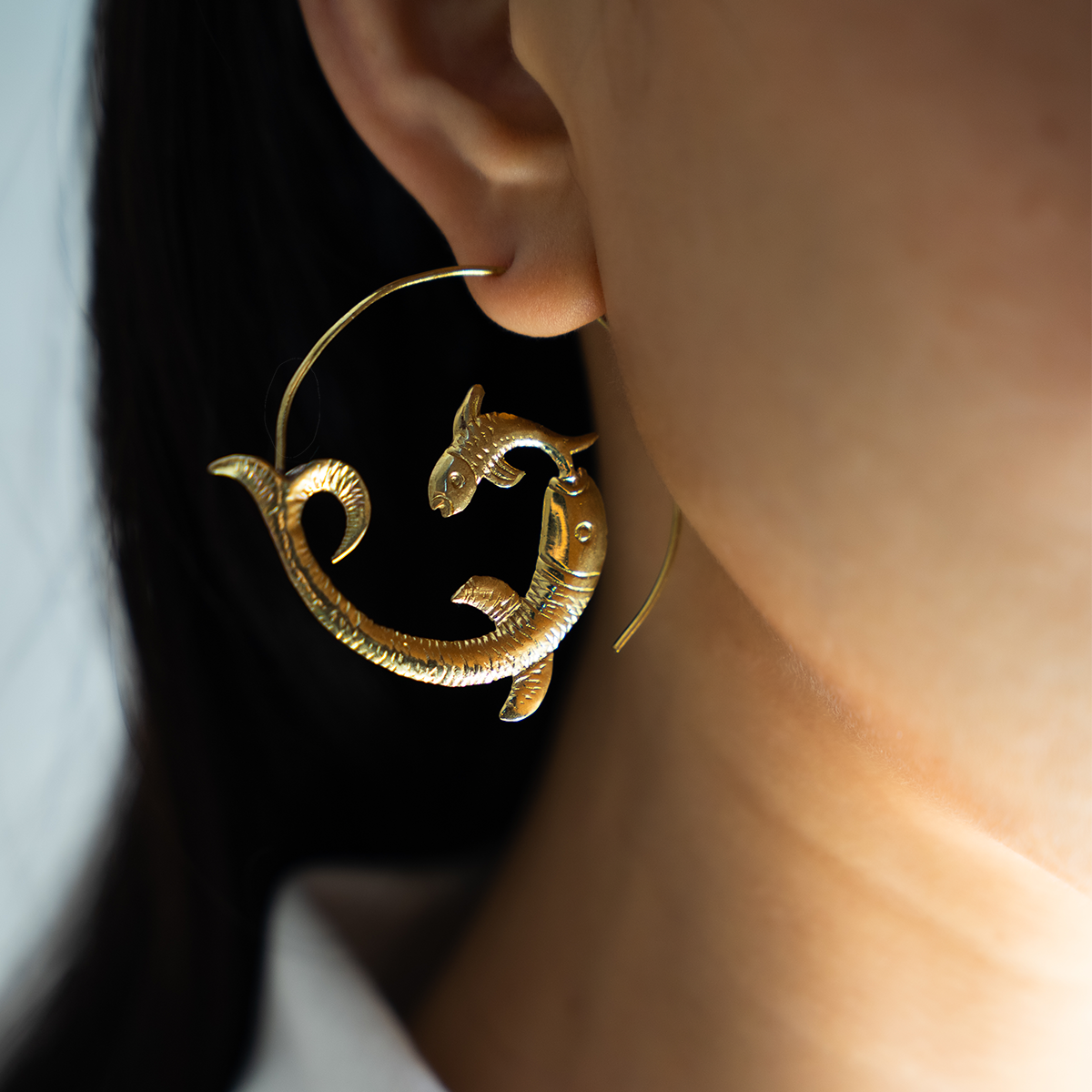 Woman wearing golden brass fish-shaped hoop earrings 