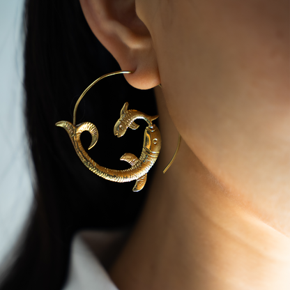 Woman wearing golden brass fish-shaped hoop earrings 