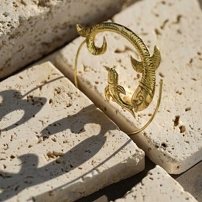 Golden brass fish-shaped hoop earrings on a stone background