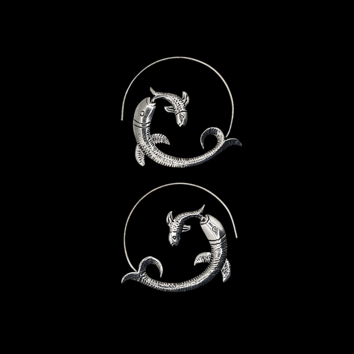 Silver fish-shaped hoop earrings on a beige background
