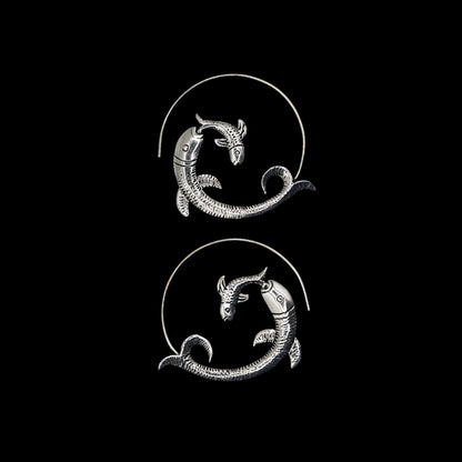 Silver fish-shaped hoop earrings on a beige background