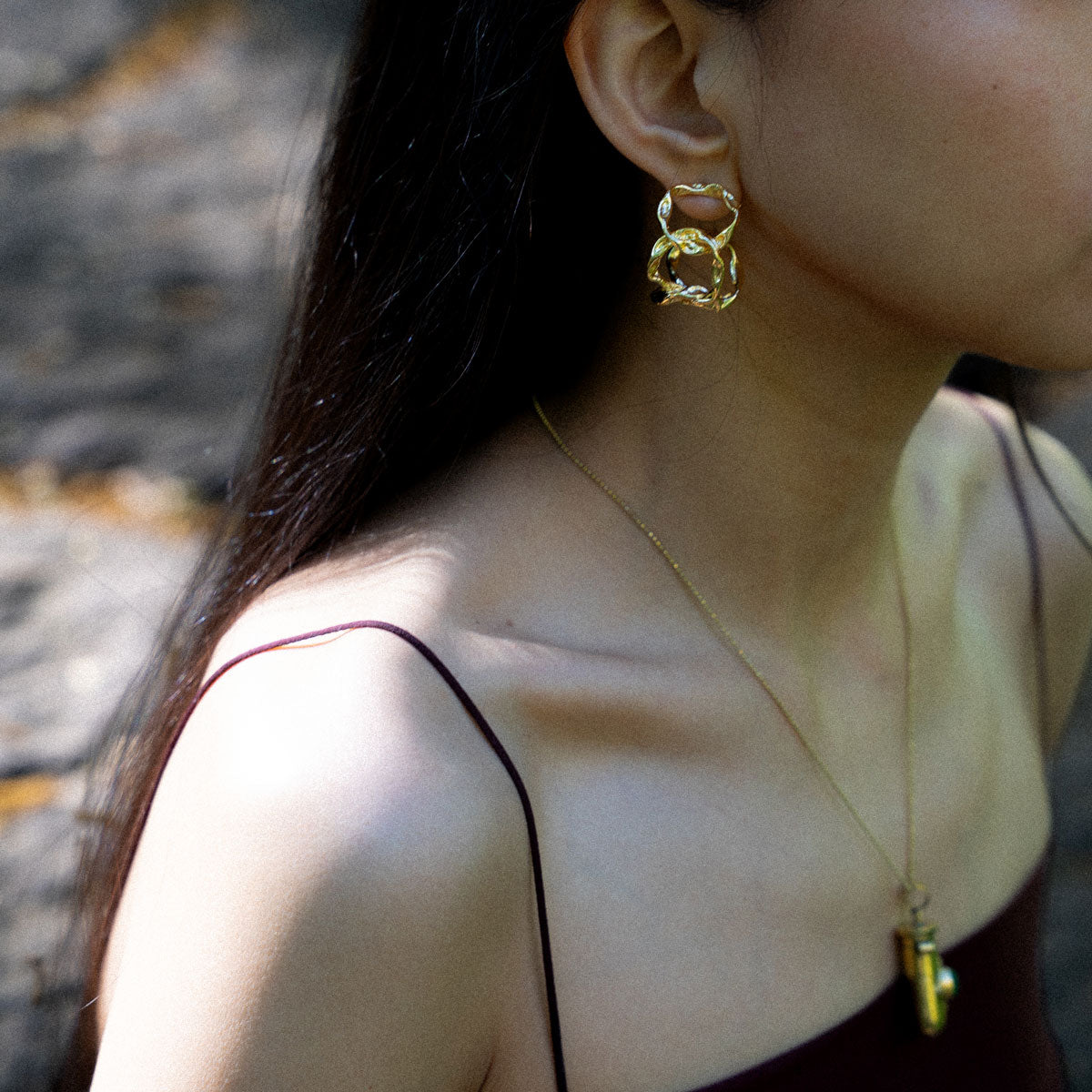 Close-up of a person wearing gold-plated hoop organic textured earrings and a golden brass pendant