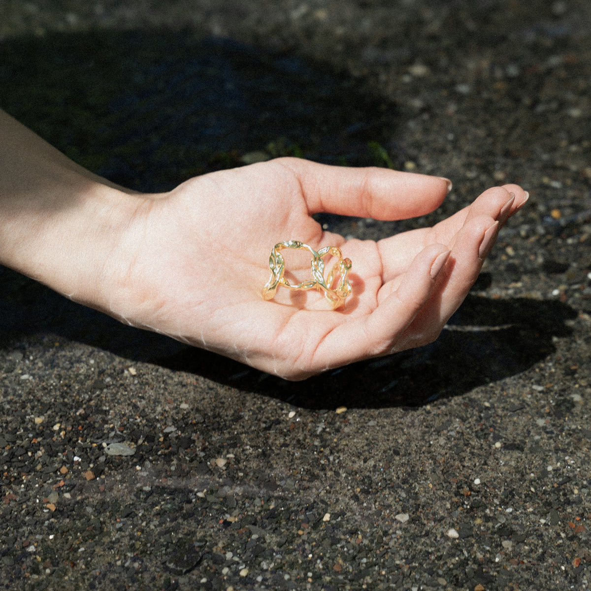 Close-up of a person's hand holding gold-plated hoop organic textured earrings