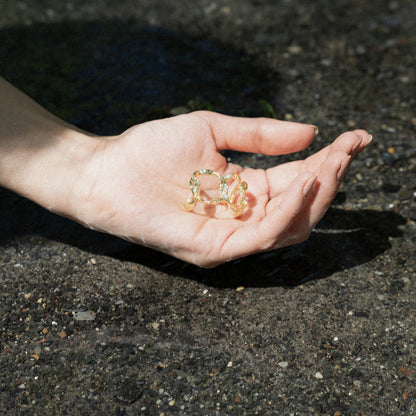 Close-up of a person's hand holding gold-plated hoop organic textured earrings