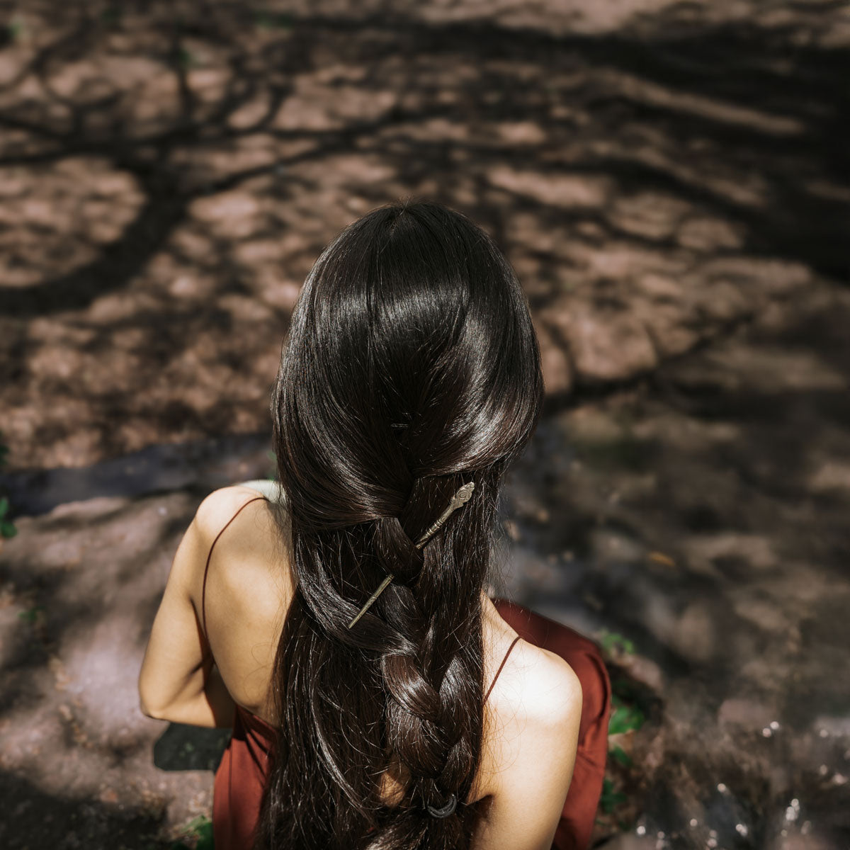 Person with a long braid sitting on the ground with a natural background with a hair pin