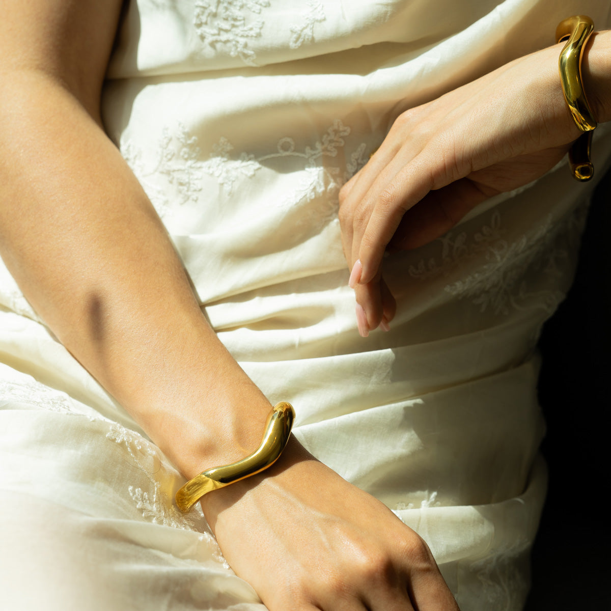 Golden fluid shaped glossy finish bracelet in set of two on a woman's wrists on a white summer dress 