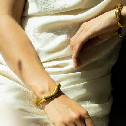 Golden fluid shaped glossy finish bracelet in set of two on a woman's wrists on a white summer dress 