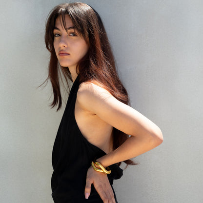 Golden fluid shaped glossy finish bracelet in set of two on a woman's wrist on a black summer dress 