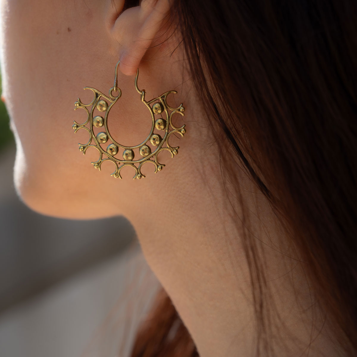 Woman wearing lightweight intricate designed earrings in a circular geometric pattern kept on stone surface