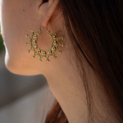 Woman wearing lightweight intricate designed earrings in a circular geometric pattern kept on stone surface
