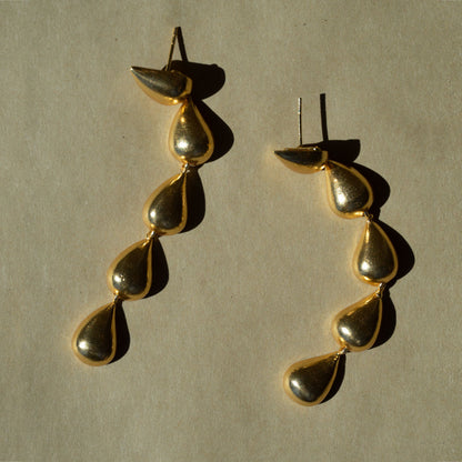 Pair of gold-plated teardrop-shaped earrings on a beige background