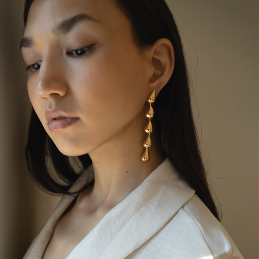 Woman wearing gold-plated long dangling drop earrings for formal ocassion