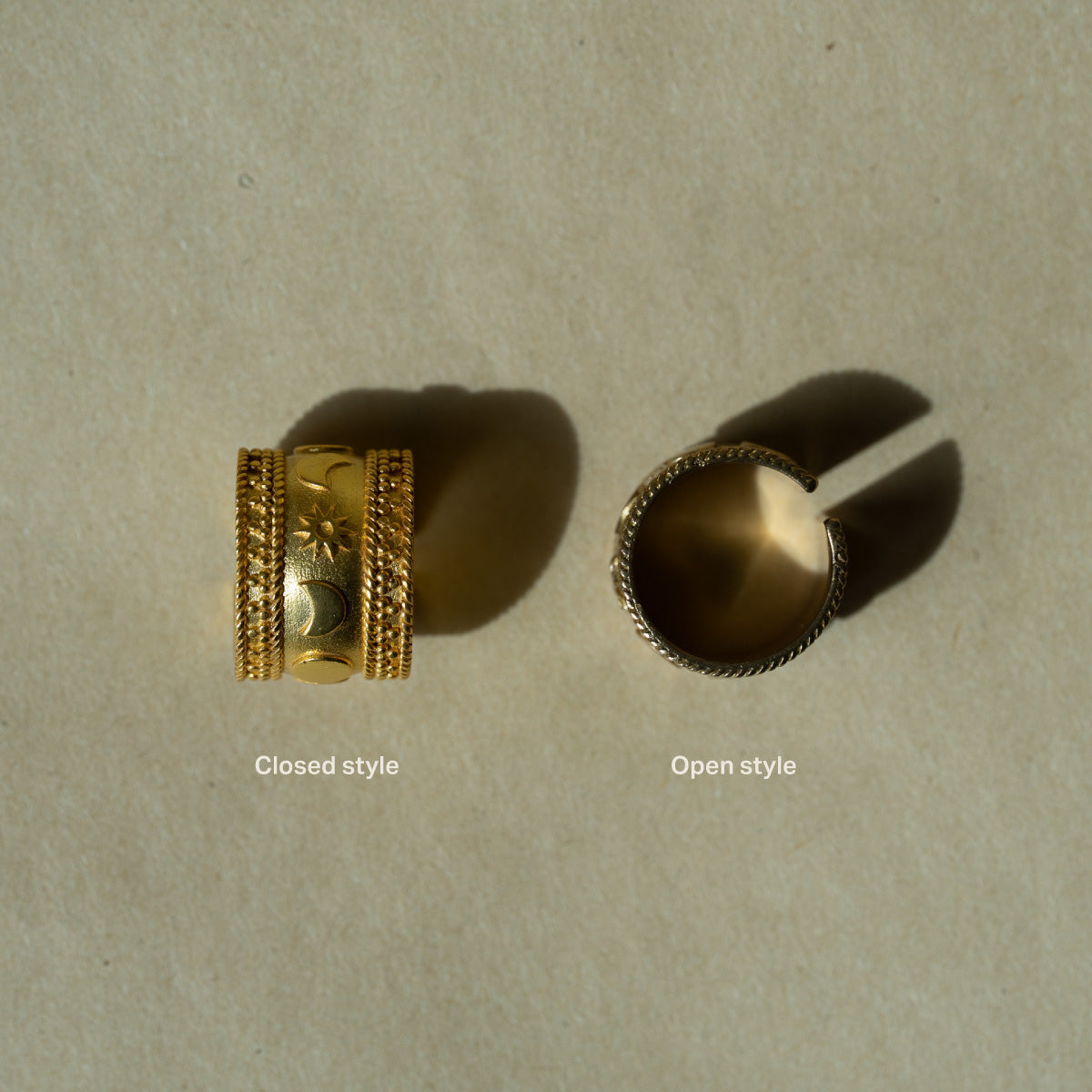 Two gold-plated rings on celestial theme sun moon stars, one closed and one open, on a beige background