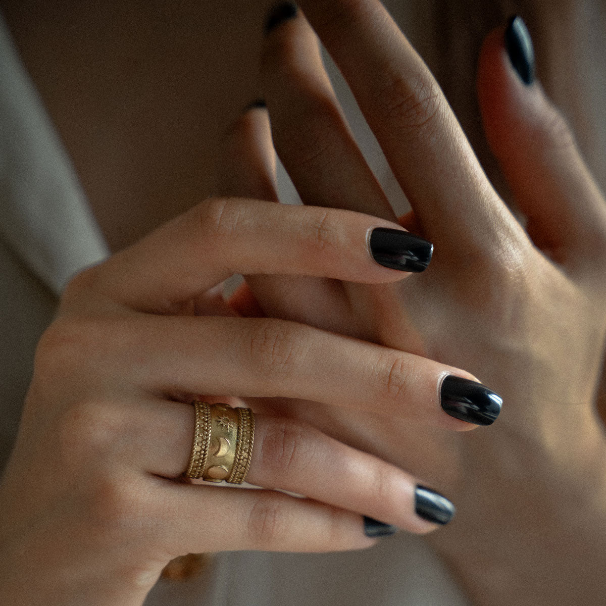Close-up of hands with gold-plated ring on celestial theme sun moon stars and black nail polish on a neutral background 