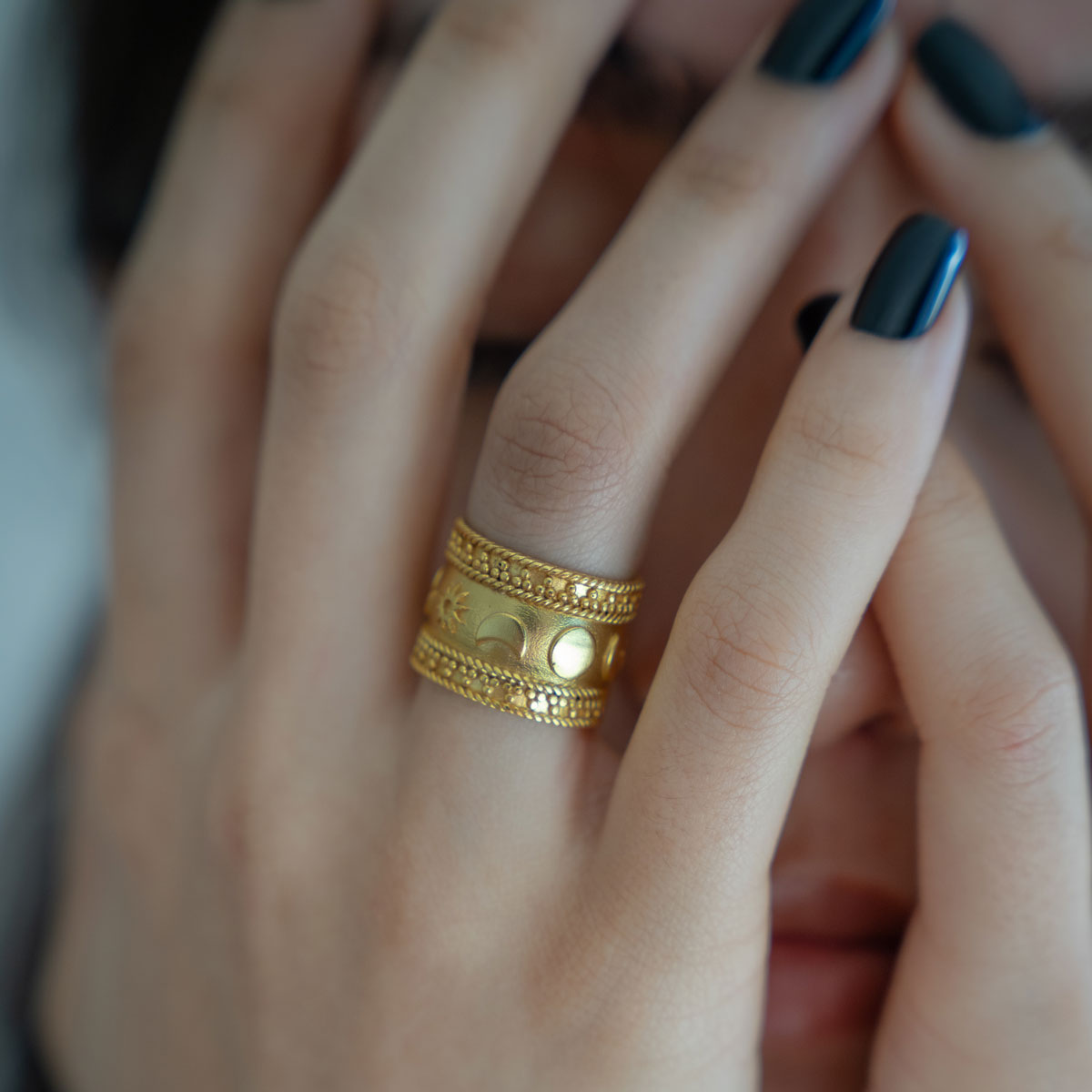 Close-up of a hand wearing a gold-plated ring on celestial theme sun moon stars with dark nail polish