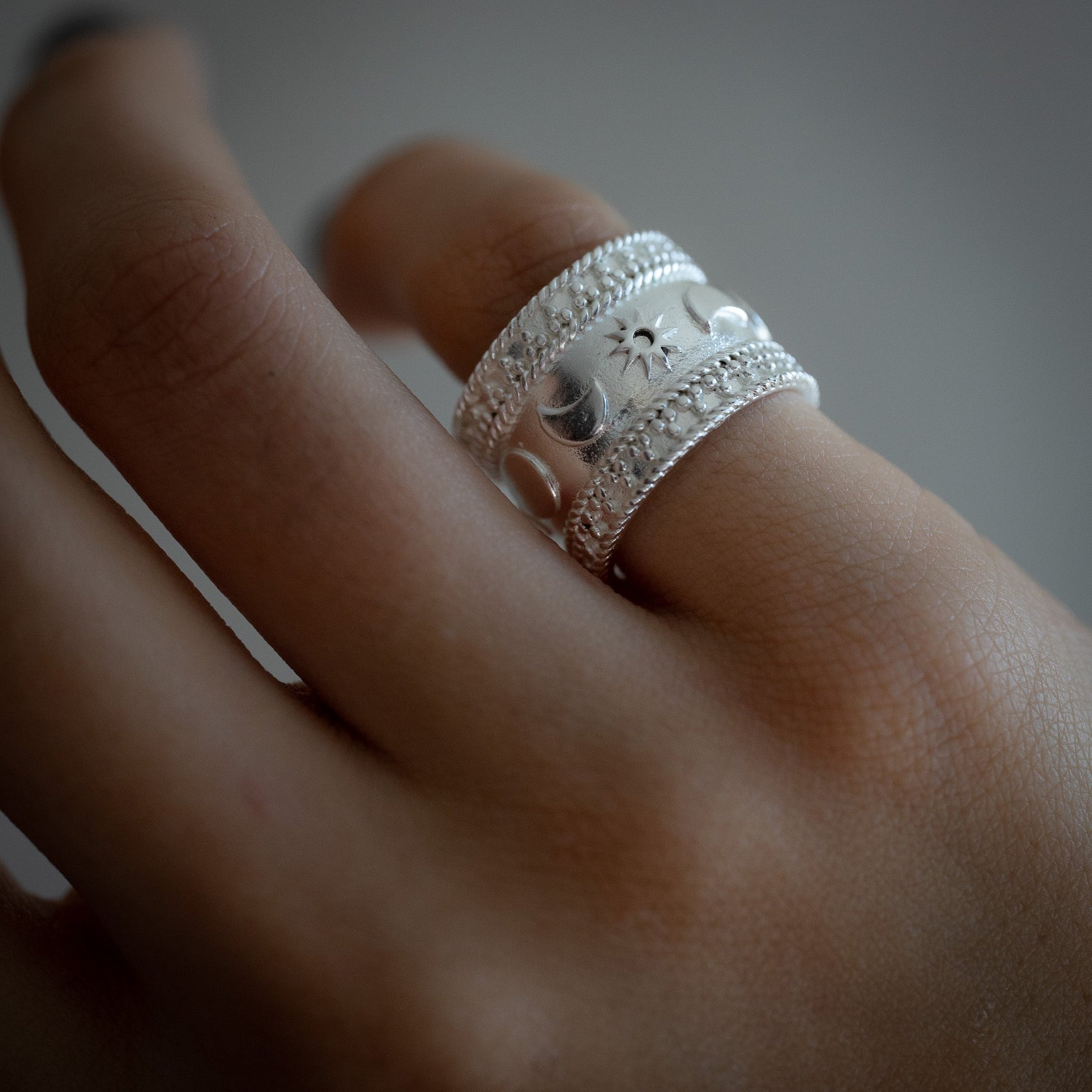 Close-up of a hand wearing a silver-plated ring with intricate designs on celestial theme sun moon stars