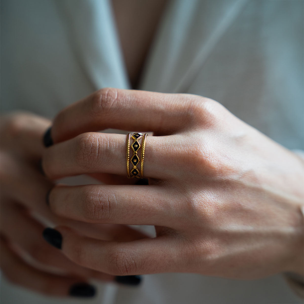 Close-up of a hand wearing a gold plated ring with a geometric design on a blurred background