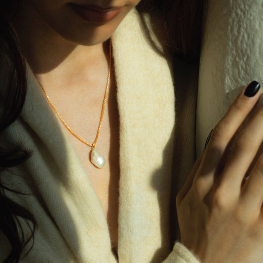 Close-up of a woman wearing a gold chain with a baroque pearl pendant