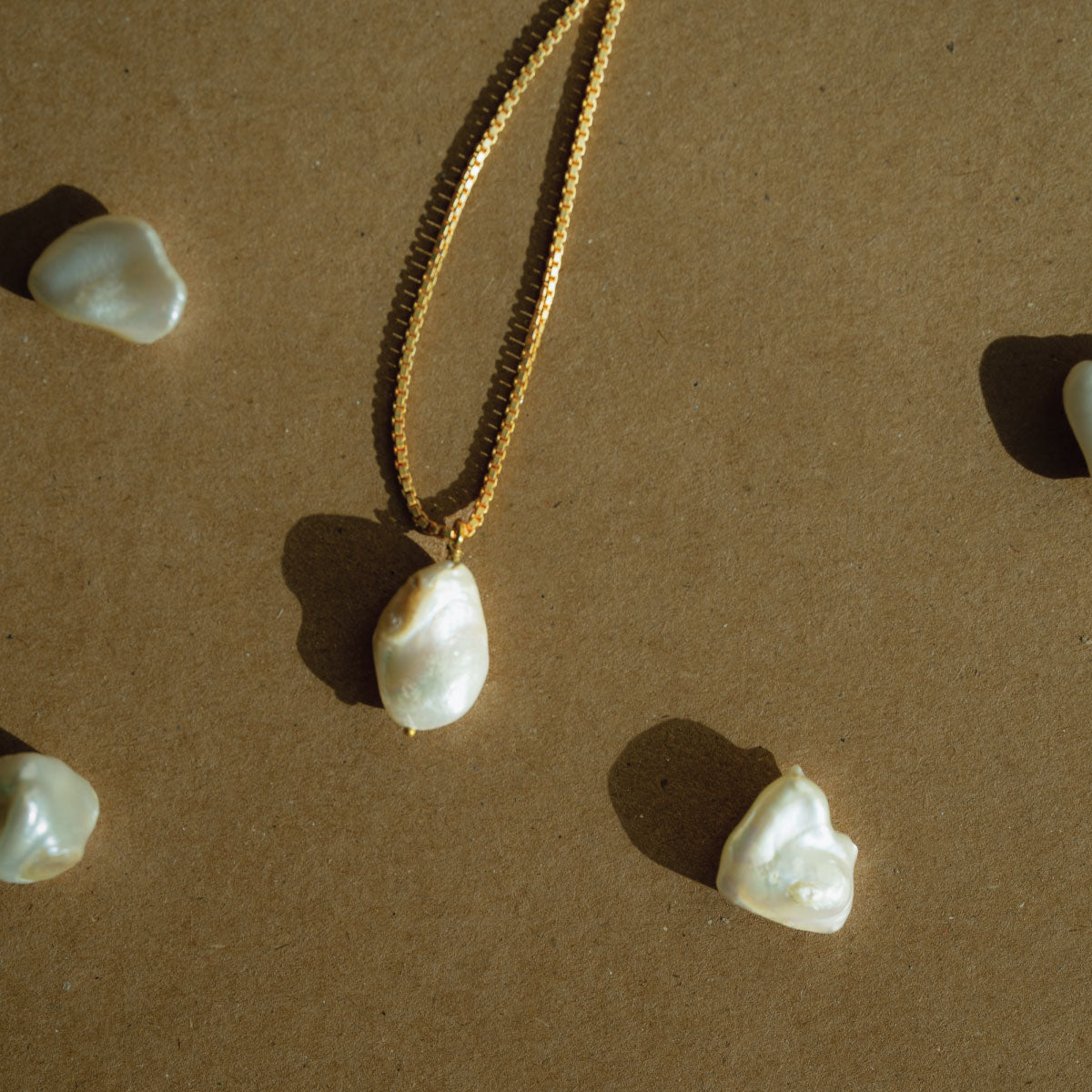 Golden chain with baroque pearl pendant on a brown background