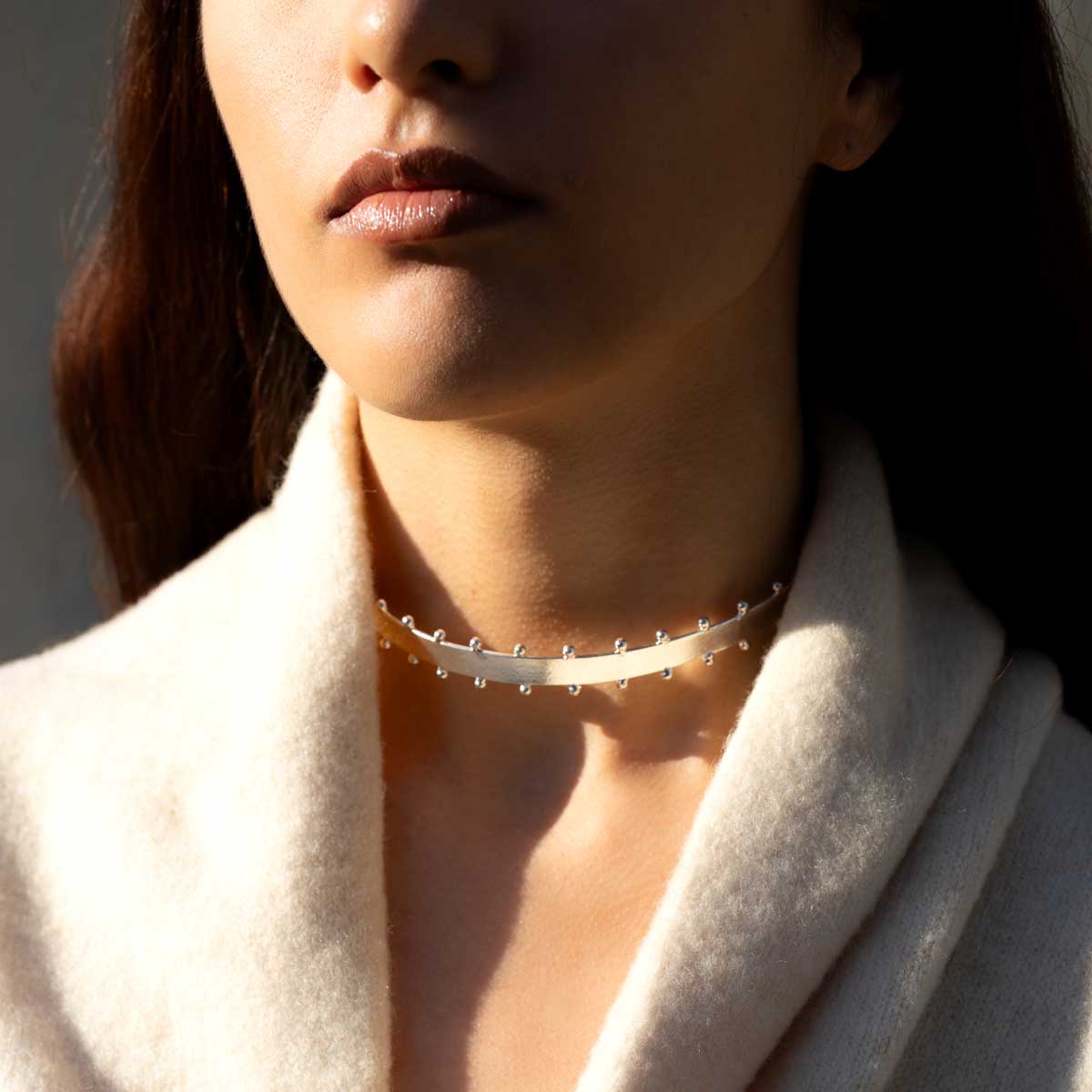 Close-up of a woman wearing a delicate silver-plated choker necklace with a soft light on their face