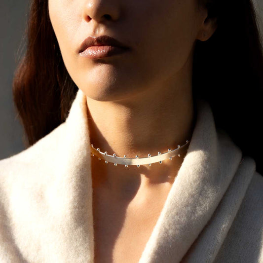 Close-up of a woman wearing a delicate silver-plated choker necklace with a soft light on their face