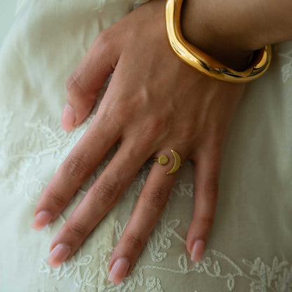 Woman wearing a gold plated geometric ring with a crescent moon and sun along with a golden bracelet on a white dress