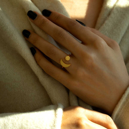 Woman wearing a gold plated geometric ring with a crescent moon and sun on a beige fabric background
