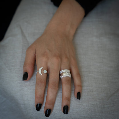 Close up of a woman's hand wearing a silver plated geometric and celestial themed rings with a crescent moon, sun and stars on a white background