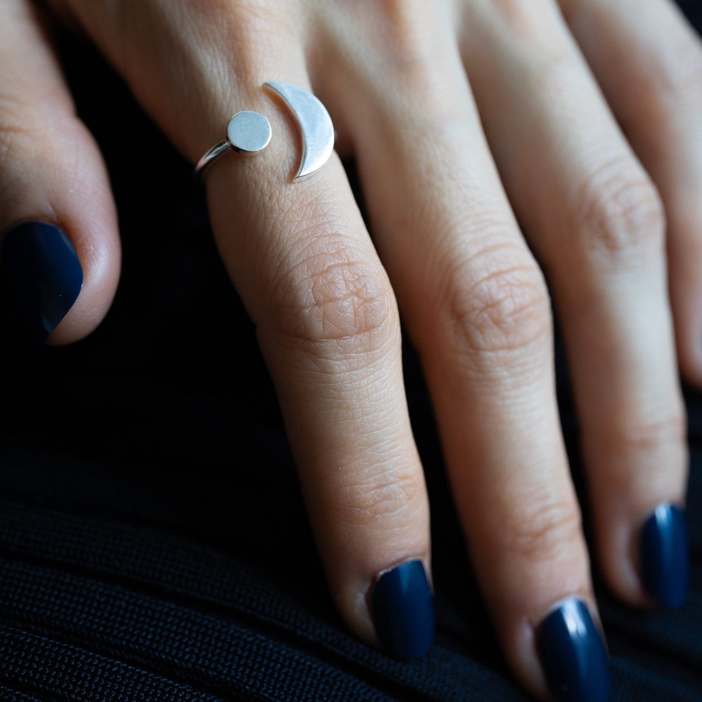 Close up of a woman's hand wearing a silver plated geometric ring with a crescent moon and sun on a black background