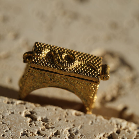 Golden antique brass poison ring with intricate snake design on a textured surface
