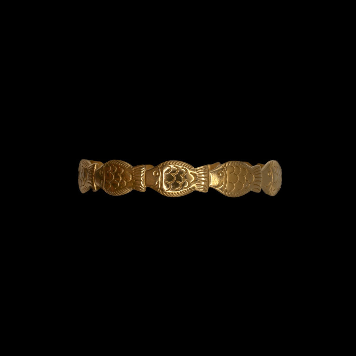 Gold bracelet with intricate fish pattern design on a black background