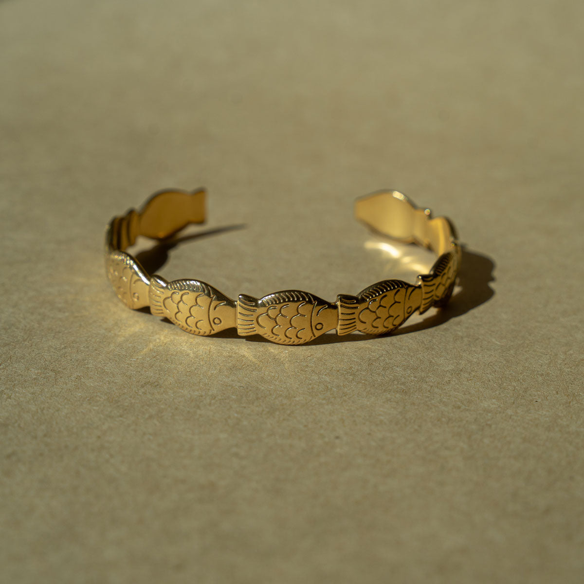 Gold plated bracelet with fish patterns on a beige background