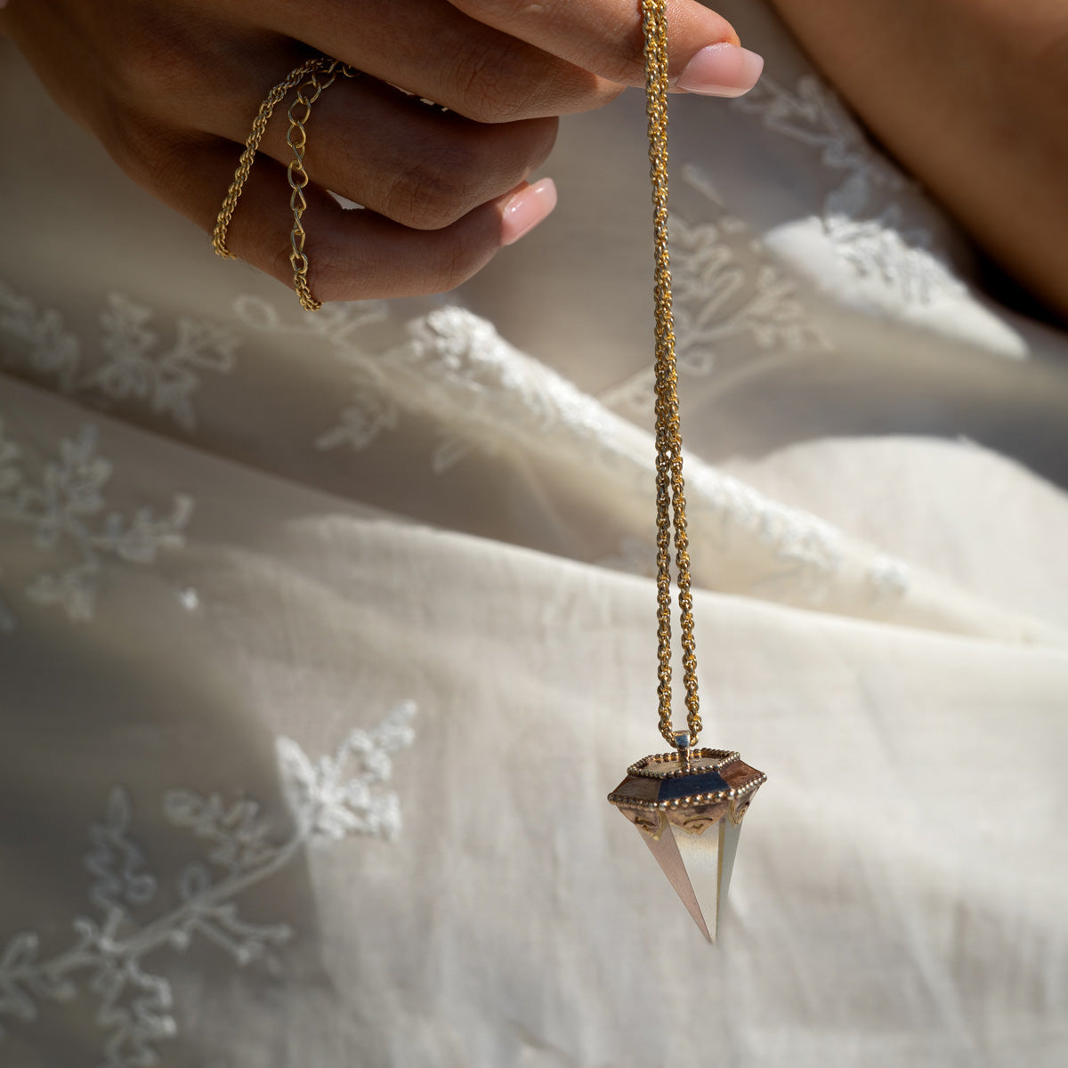 Close-up of a hand holding a crystal pendulum pendant