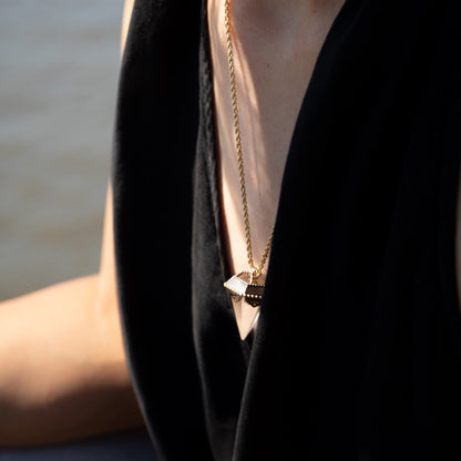 Person wearing a black summer dress with a golden necklace featuring a crystal pendant