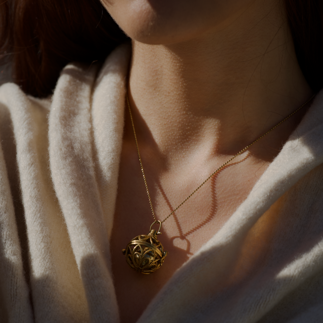 Close-up of a person wearing a golden orb shaped pendant necklace made in brass