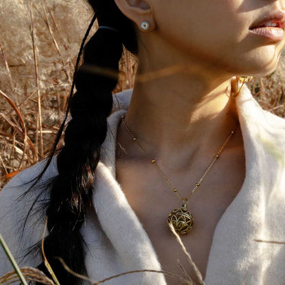 Woman wearing a golden orb shaped pendant necklace made in brass