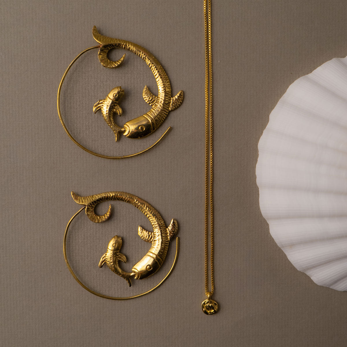 Golden brass fish-shaped hoop earrings and pendant set on a beige background