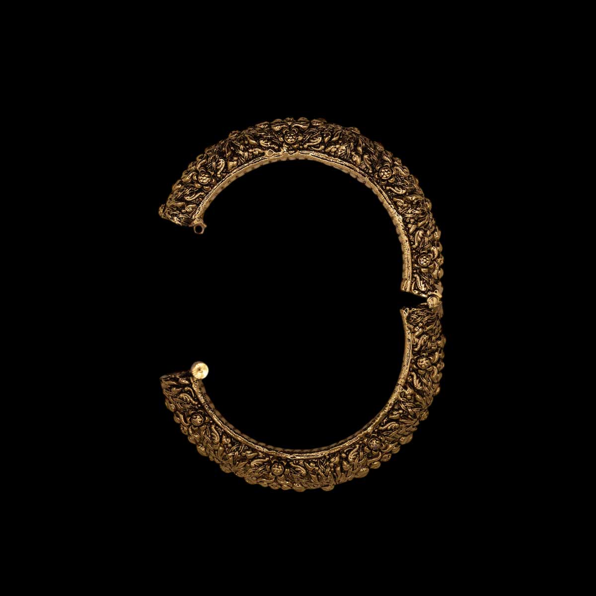 Open view of antique ornate brass indian golden bracelet with intricate engravings on a black background