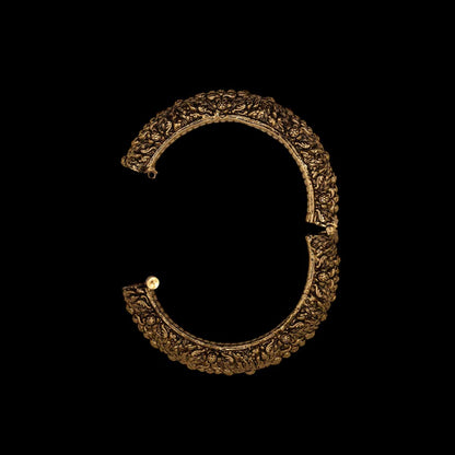 Open view of antique ornate brass indian golden bracelet with intricate engravings on a black background